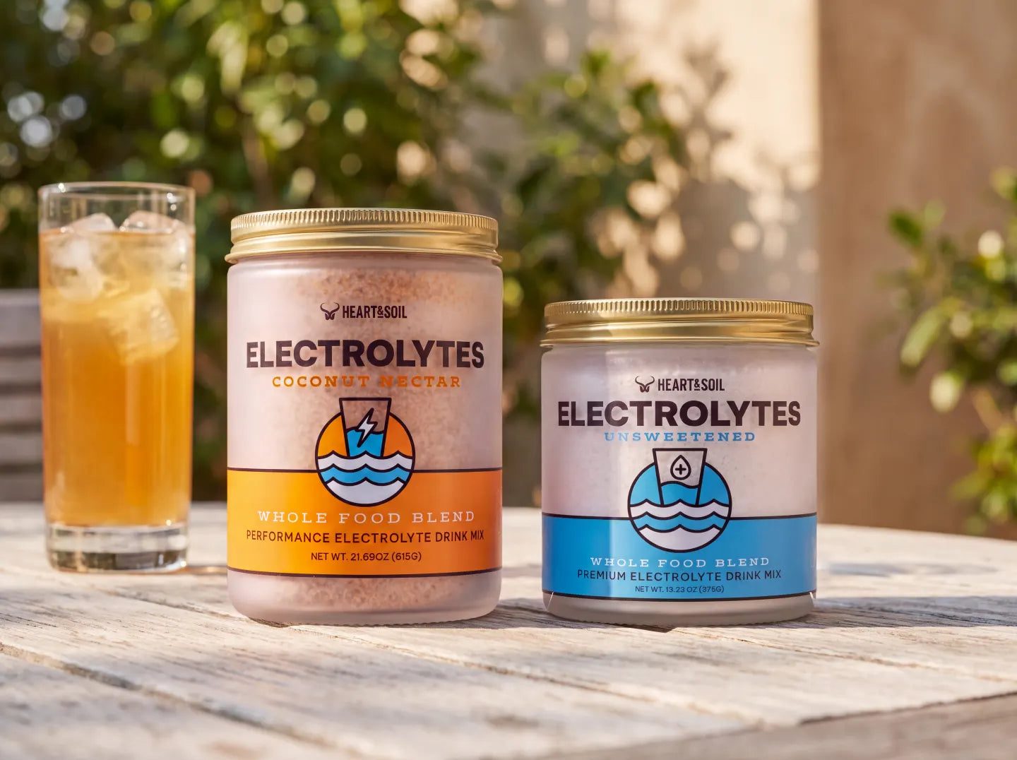 Heart & Soil Electrolytes Coconut Nectar and Unsweetened jars on an outdoor table beside an iced glass
