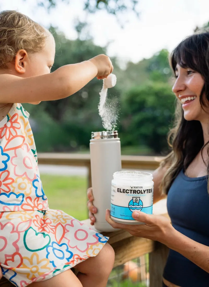 A child pours a scoop of Electrolytes into a water bottle as a woman smiles